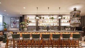 Una zona de bar con suelo de baldosas, una barra repleta de botellas y varias sillas con asientos acolchados.
