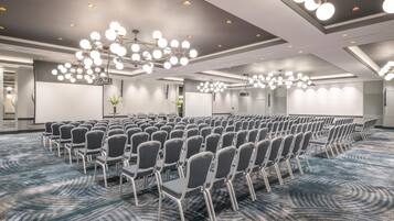 Un salón de conferencias con filas de sillas, luces en el techo y piso alfombrado.