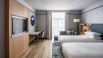 Habitación de hotel con dos camas, un escritorio, un televisor y vistas a la ciudad.