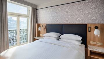 Camera d'albergo con un letto grande, una testiera in legno, un comodino con una lampada e vista su un balcone.
