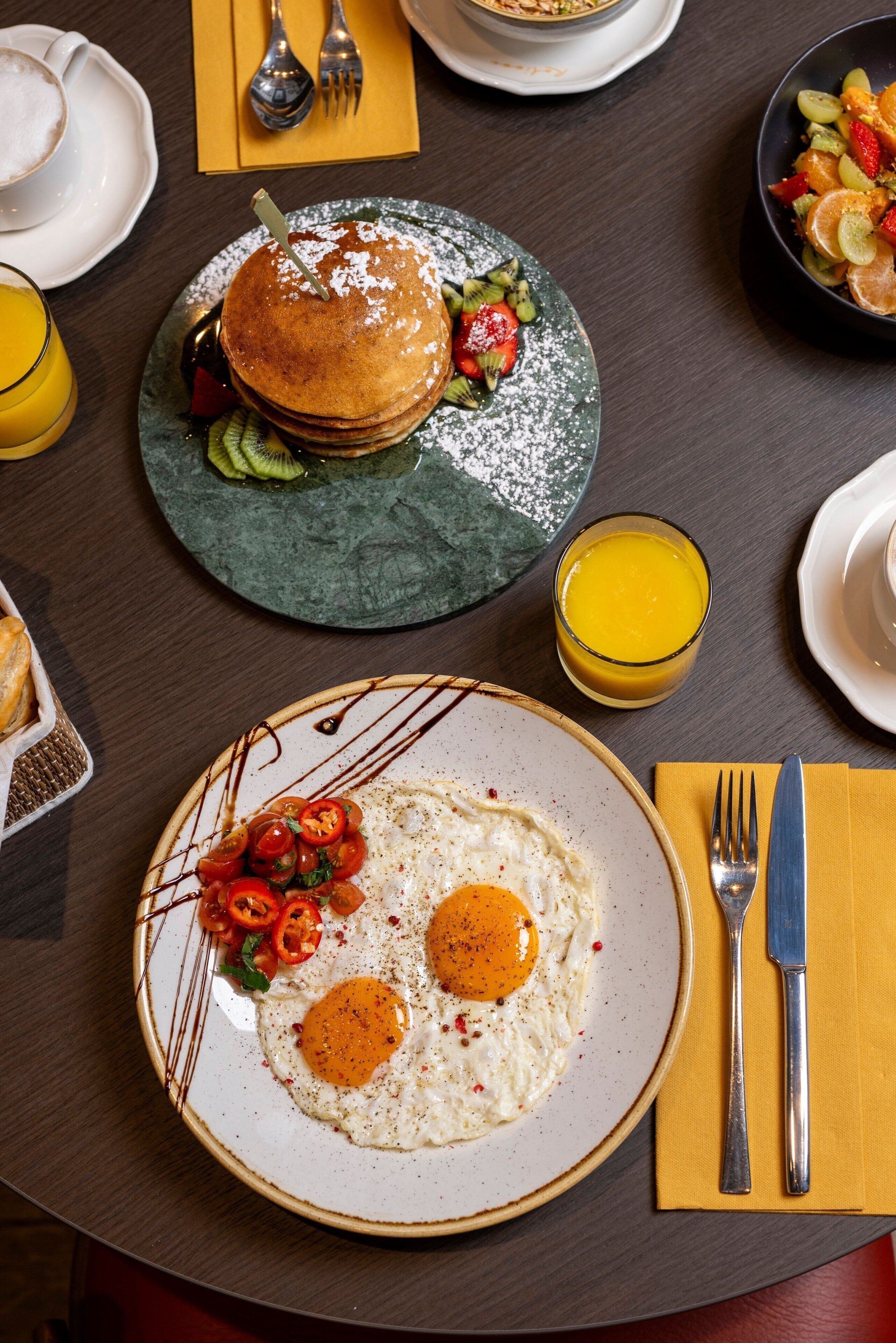 A breakfast setting with pancakes, eggs, and a glass of orange juice on a table.
