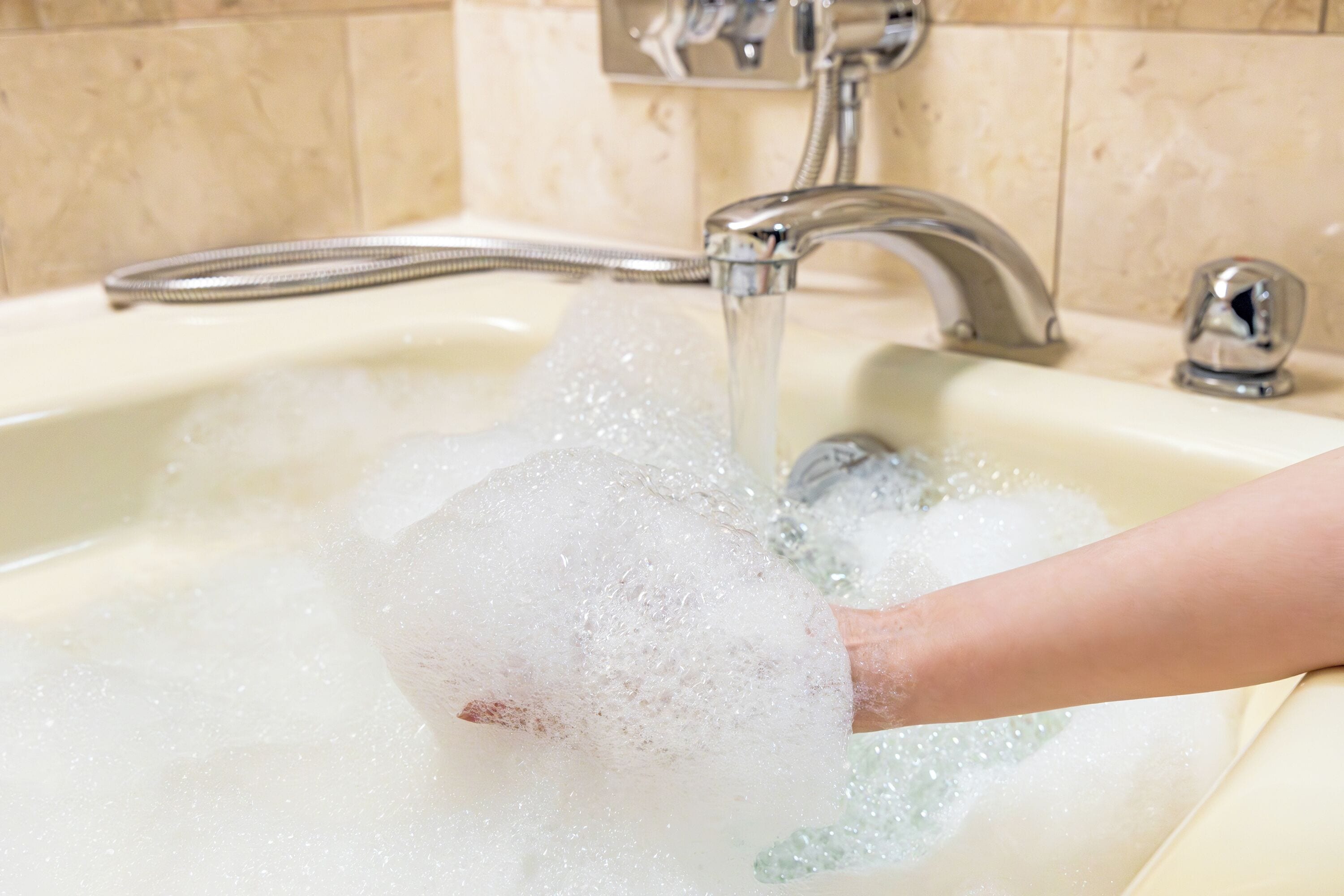 A hand holding a bubble under a running tap in a bathroom sink.