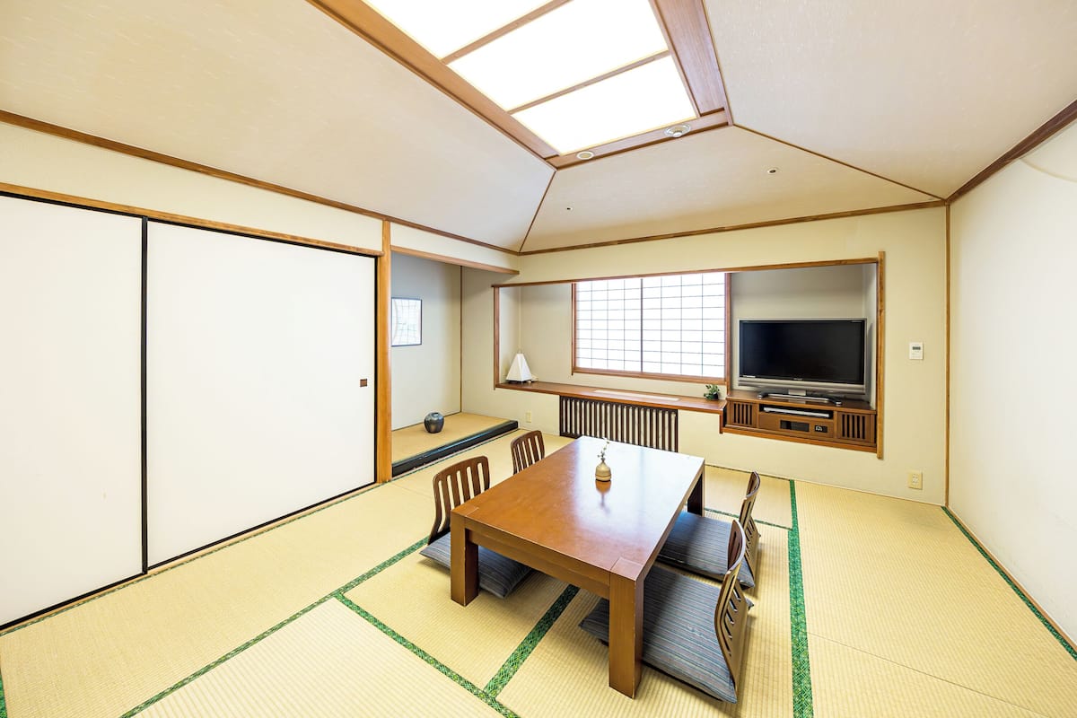 Une pièce de style japonais traditionnel, avec un sol recouvert de tatamis, une petite table en bois et un téléviseur fixé au mur.