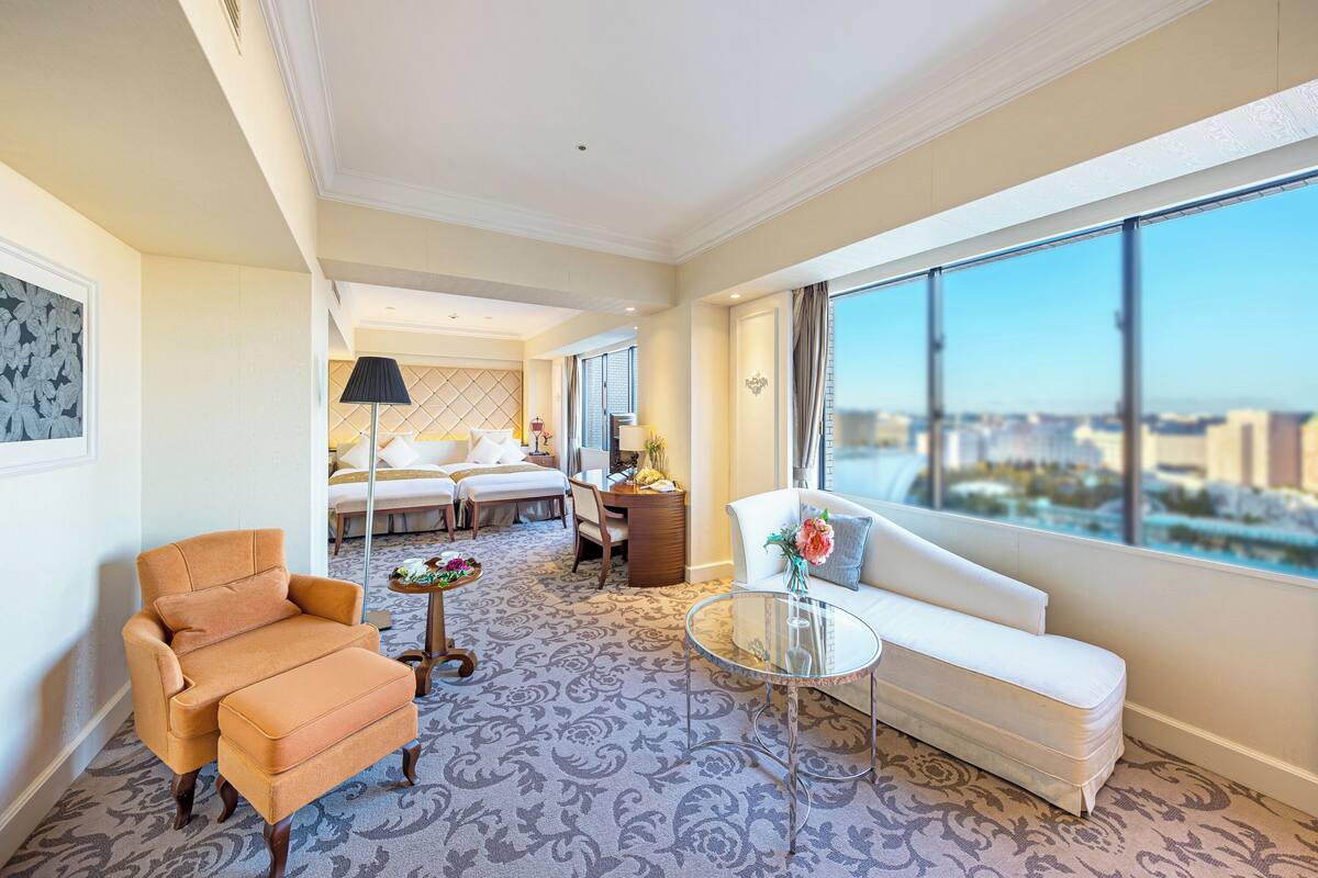 Une chambre d’hôtel avec une grande fenêtre, un canapé, un fauteuil, une petite table et une lampe décorative.