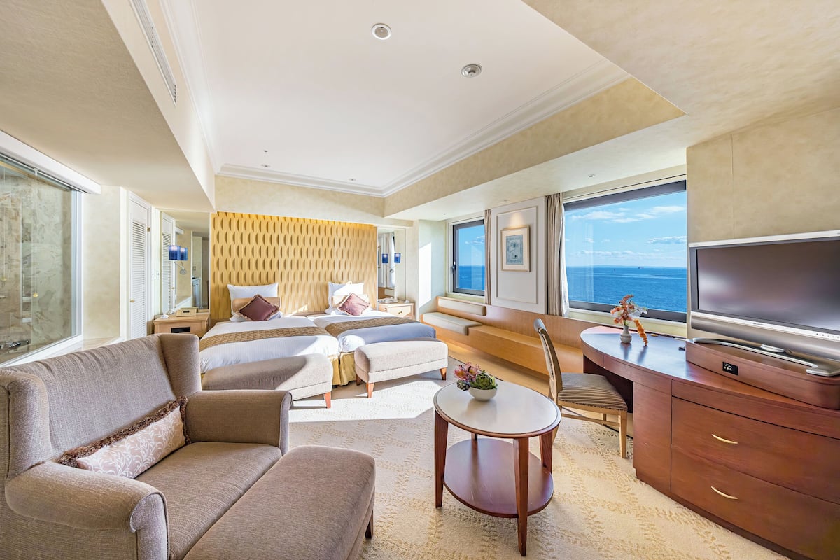Une chambre d’hôtel spacieuse, dotée d’un grand lit, d’un canapé, d’un bureau avec une télévision et offrant une vue sur la mer.