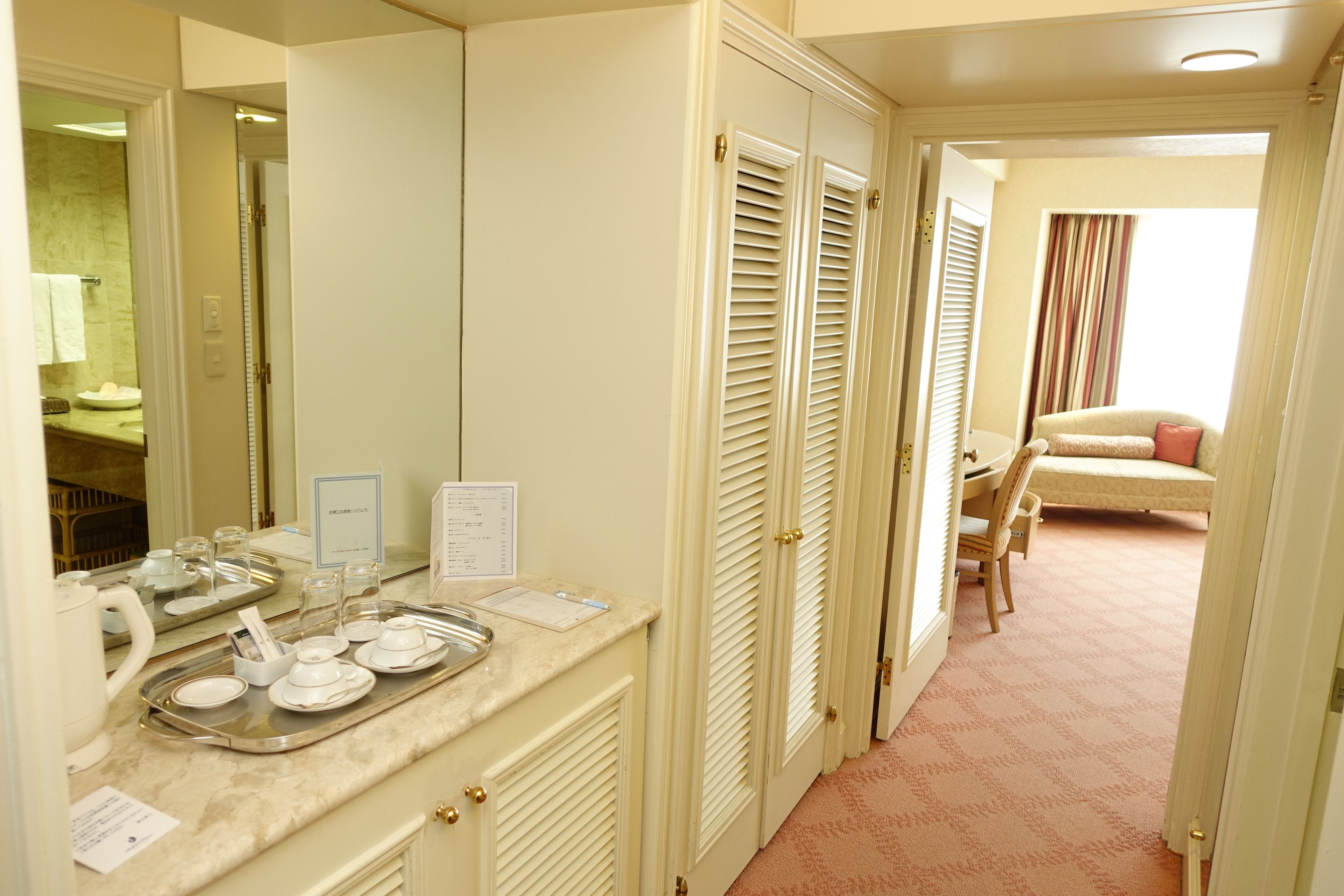 Een hotelkamer met een badkamer, een zithoek met een tafel en stoelen, en een bed met een gestreept gordijn.