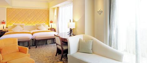 A hotel room with two beds, a sofa, a chair, a desk, and a large window with curtains.