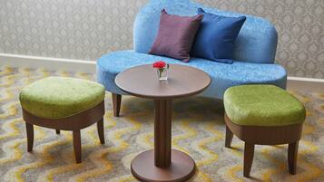 Una habitación con un sofá azul, dos otomanas verdes y una mesa redonda de madera con un jarrón de flores.