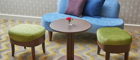 A room with a blue sofa, two green ottomans, and a round wooden table with a vase of flowers.