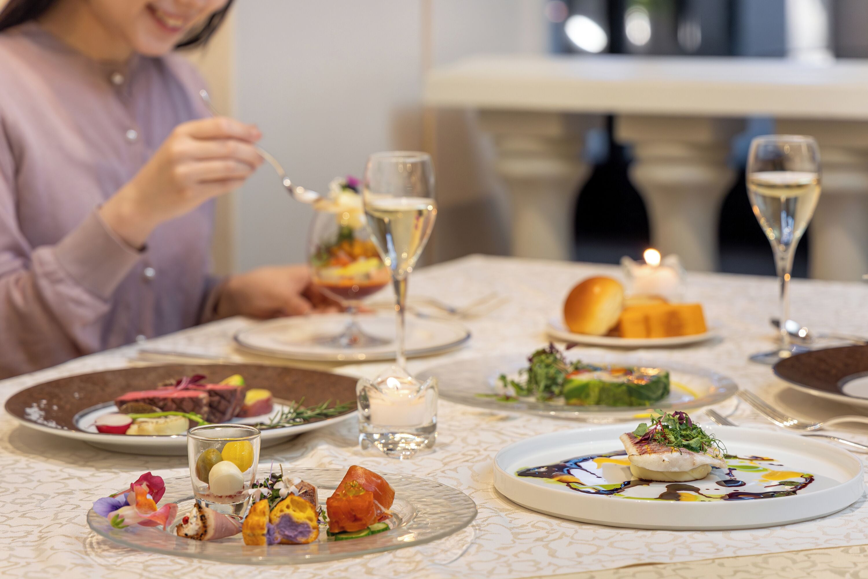 A dining table with various dishes and glasses of wine.