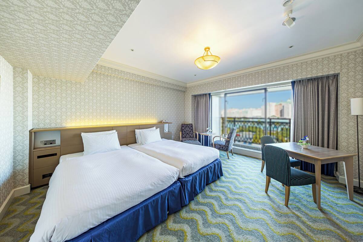 Une chambre d’hôtel avec un grand lit, un bureau et une chaise. Il y a une fenêtre donnant sur la ville.