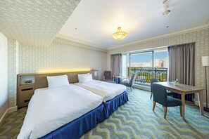 A hotel room with a large bed, a desk, and a chair. There is a window with a view of the city.