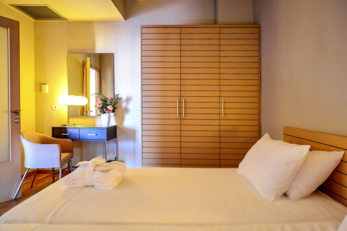 A hotel room with a bed, a desk, a chair, a wardrobe, and a mirror.