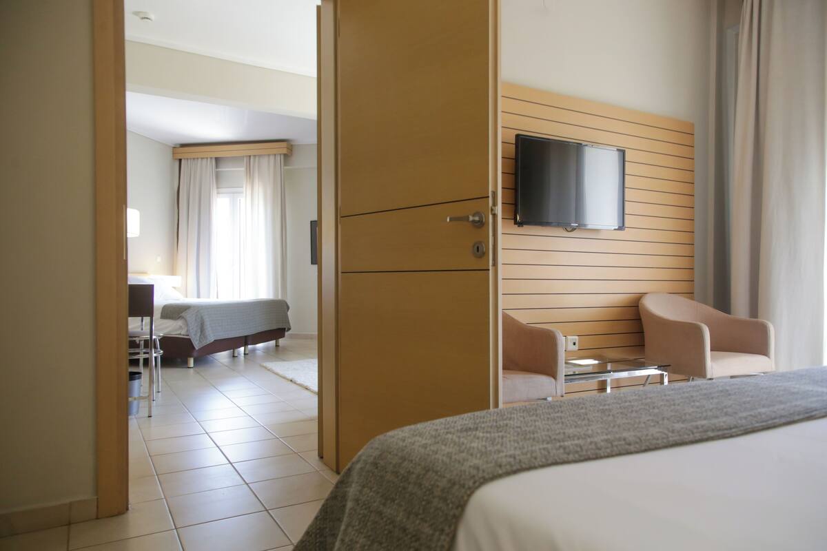 A hotel room with a bed, a desk, a chair, a TV mounted on the wall, and a window with curtains.