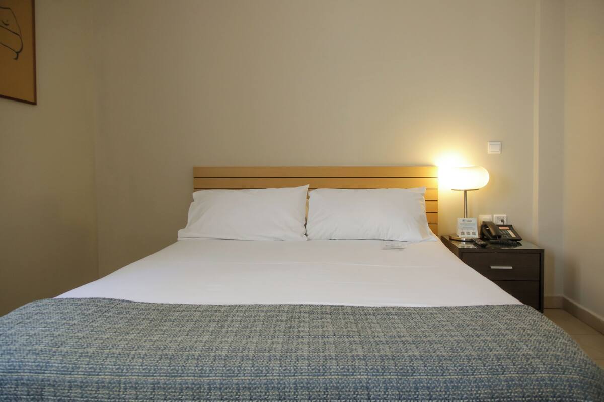 A hotel room with a large bed, a bedside table with a lamp, and a telephone.