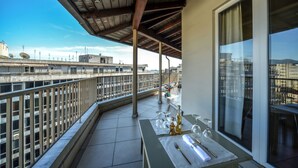 A balcony with a table set for dining, a view of the cityscape, and a pergola overhead.
