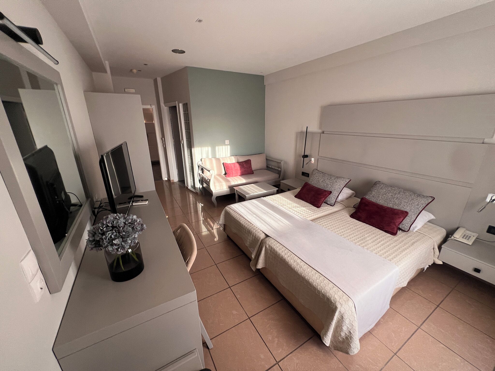 A modern hotel room with a large bed, a desk with a computer, a TV, and a bathroom visible through an open door.