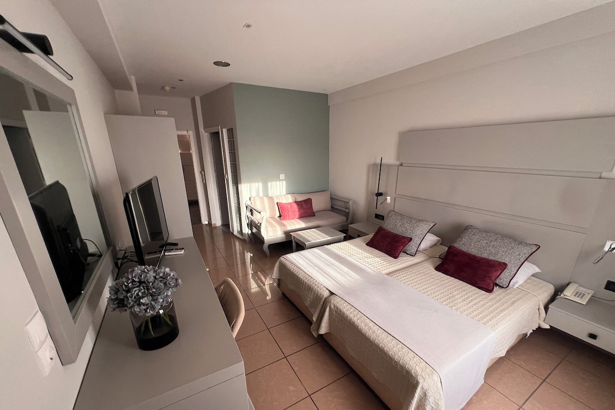 A modern hotel room with a large bed, a desk with a computer, a TV, and a bathroom visible through an open door.