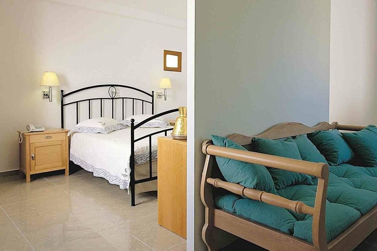 Een kamer met een bed, nachtkastje, lamp en een lijst aan de muur.
