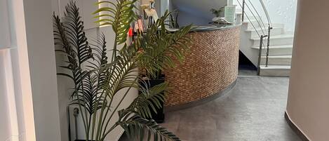A modern hotel lobby with a reception desk, a staircase, and a seating area with a sofa and a plant.
