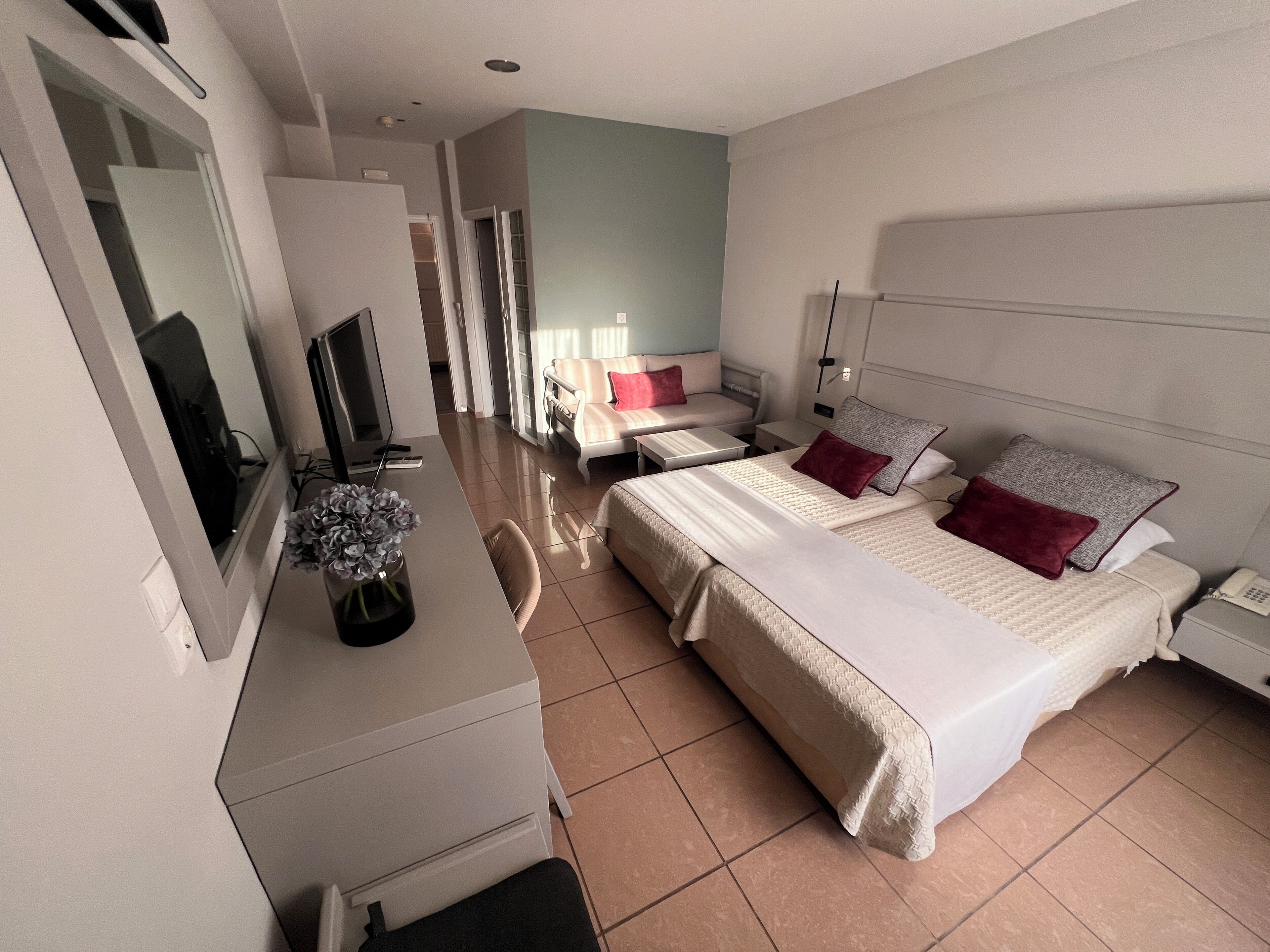 Una habitación de hotel con cama, escritorio, silla, televisión y un florero con flores.