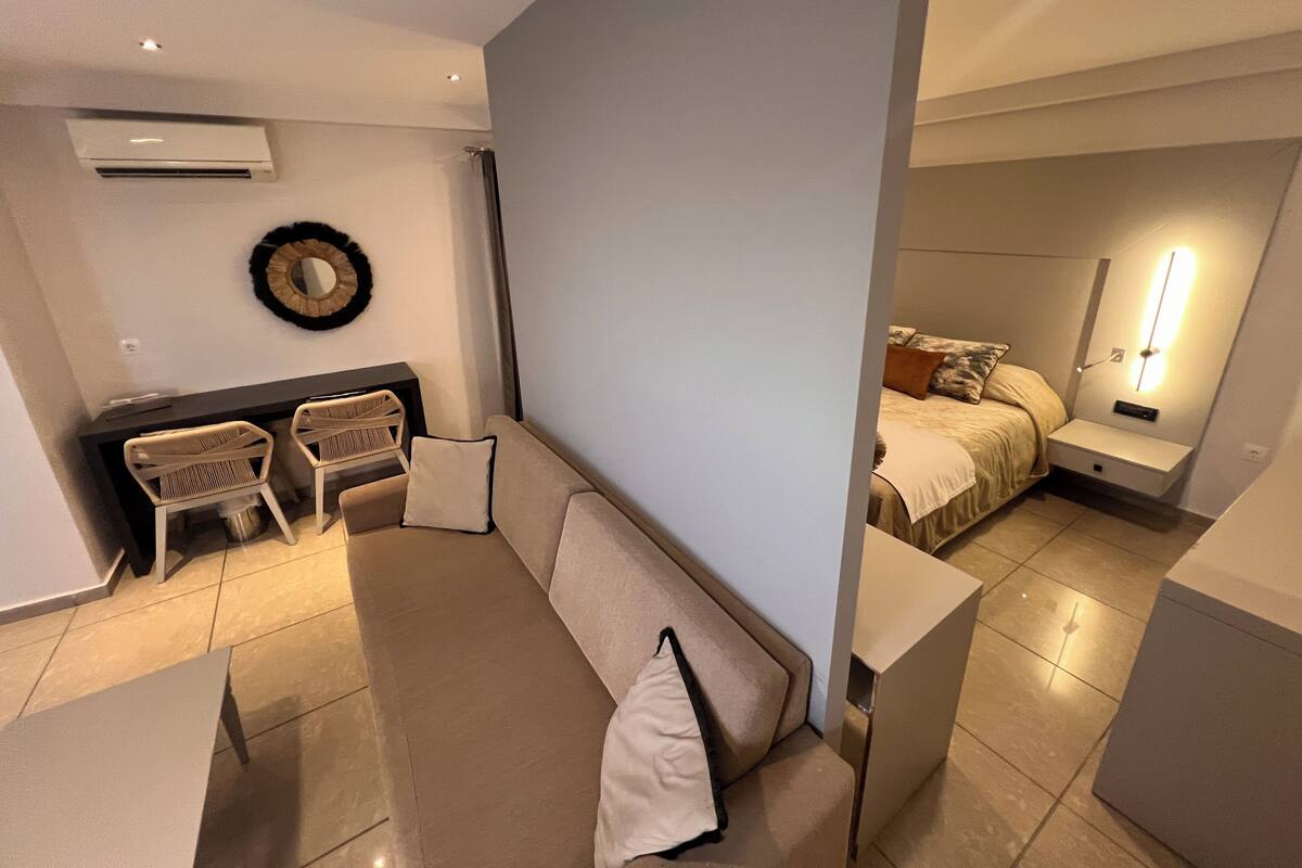 Een moderne woonkamer met een bank, stoelen, een klein tafeltje en een bed met nachtkastje.