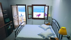 Ein Schlafzimmer mit Bett, Nachttischlampe, Telefon und Meerblick durch ein offenes Fenster.