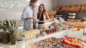 A buffet with various food items and beverages, a man and a woman standing by the counter, and a modern interior design. - Aressana Spa Hotel & Suites - Small Luxury Hotels of the World (Santorini)