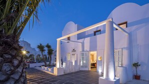A modern hotel entrance with a white facade, large columns, and a palm tree in the foreground. - Aressana Spa Hotel & Suites - Small Luxury Hotels of the World (Santorini)
