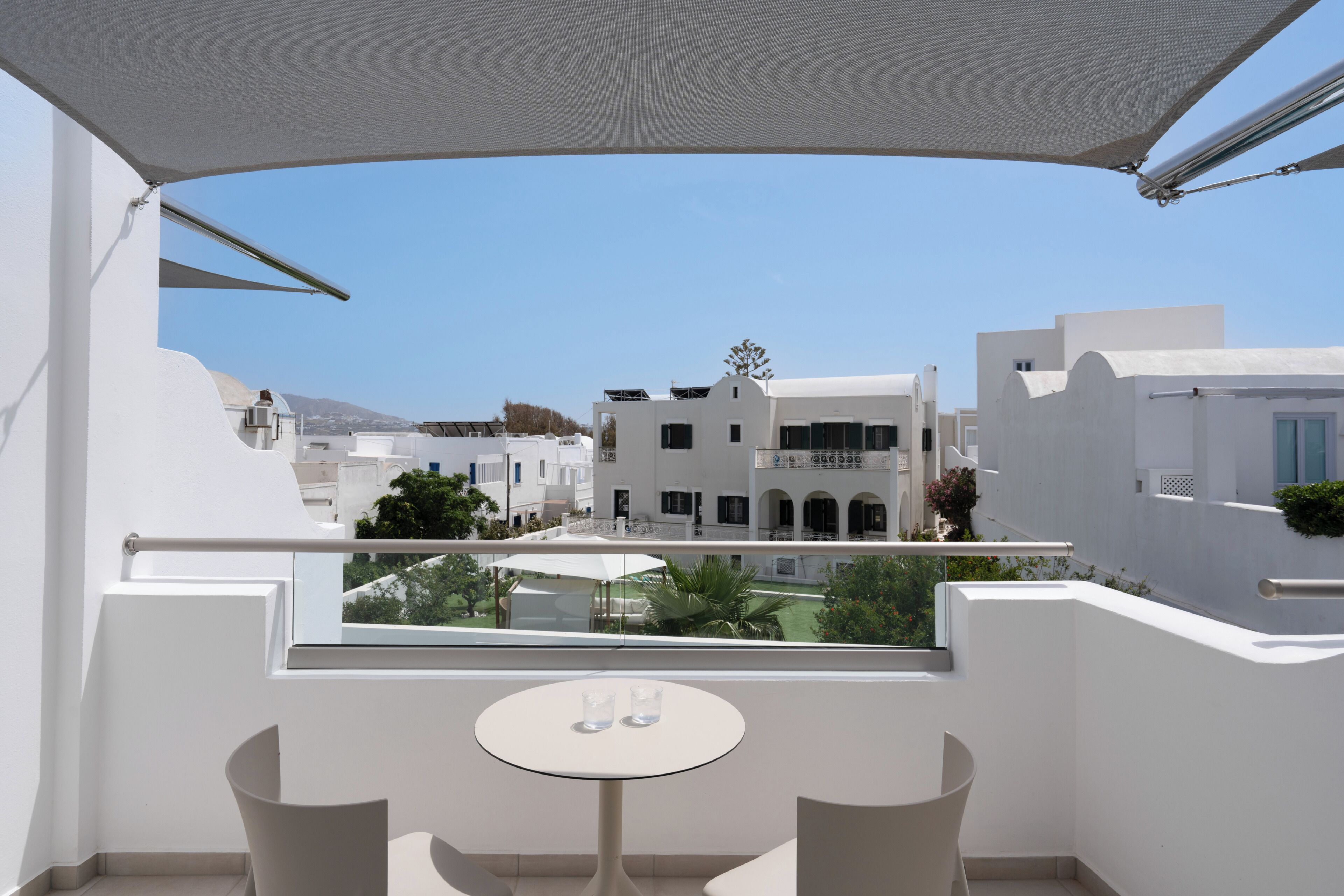 Un balcón con mesa y sillas, con vista a un patio interior con edificios y una montaña al fondo.