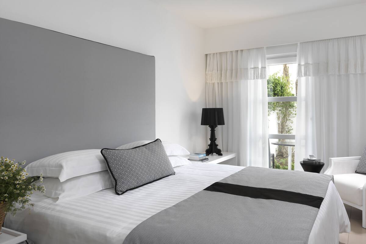 Een moderne hotelkamer met een groot bed, een nachtkastje met een lamp, een stoel en een raam met gordijnen.