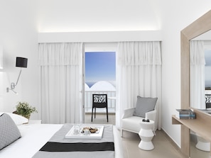 A modern hotel room with a bed, a sitting area with a chair and a small table, a balcony with a view, and a large mirror.