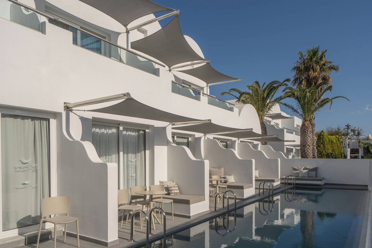 Een modern hotel met een zwembad, terras en palmbomen.