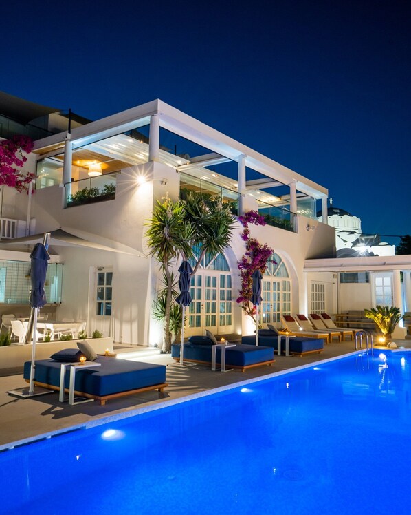 A modern hotel with a pool, outdoor seating, and a view of a white building in the background.