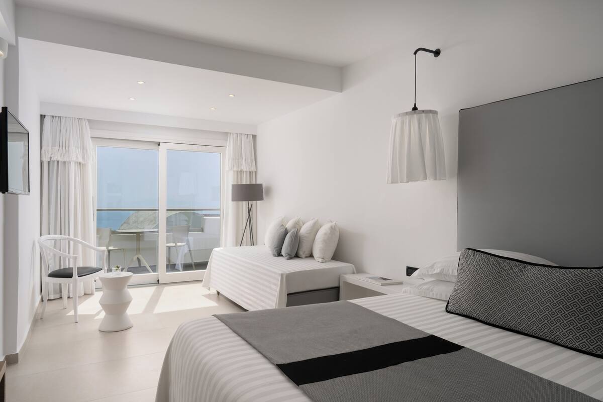 Een moderne hotelkamer met een groot bed, een apart zithoekje met een stoel, een klein tafeltje en een balkon met uitzicht.