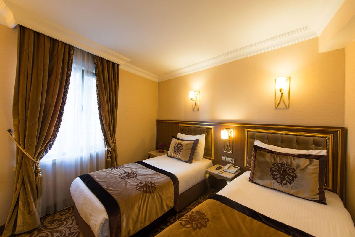 Ein Hotelzimmer mit zwei Betten, einem Nachttisch, einer Lampe und einem Fenster mit Vorhängen.