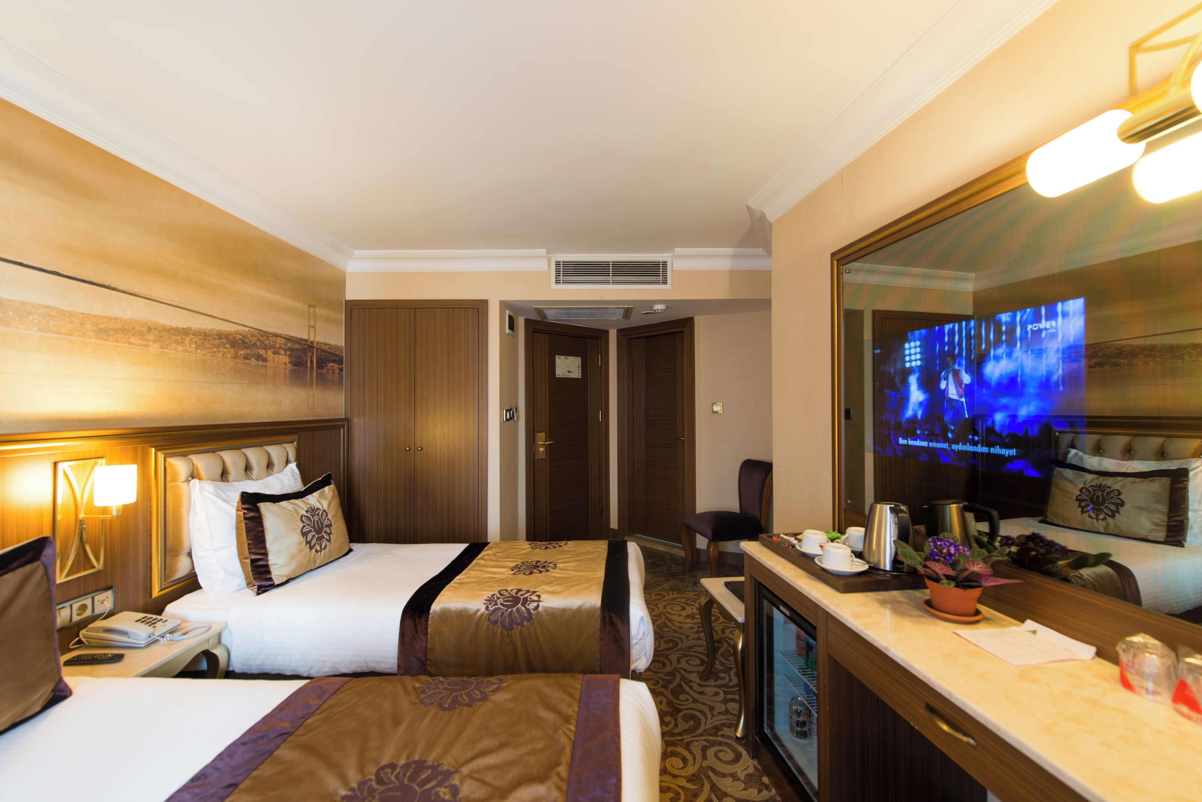 Una habitación de hotel con dos camas, un escritorio con cafetera, televisión y un espejo grande.