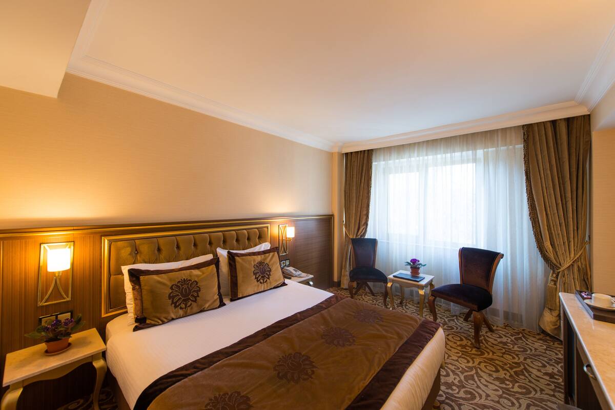 Ein Hotelzimmer mit einem großen Bett, einem Schreibtisch, einem Stuhl und einem Fenster mit Vorhängen.