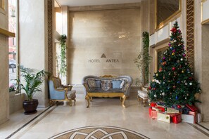 Um lobby com um sofá, uma árvore de Natal e uma placa indicando "HOTEL ANTEA".