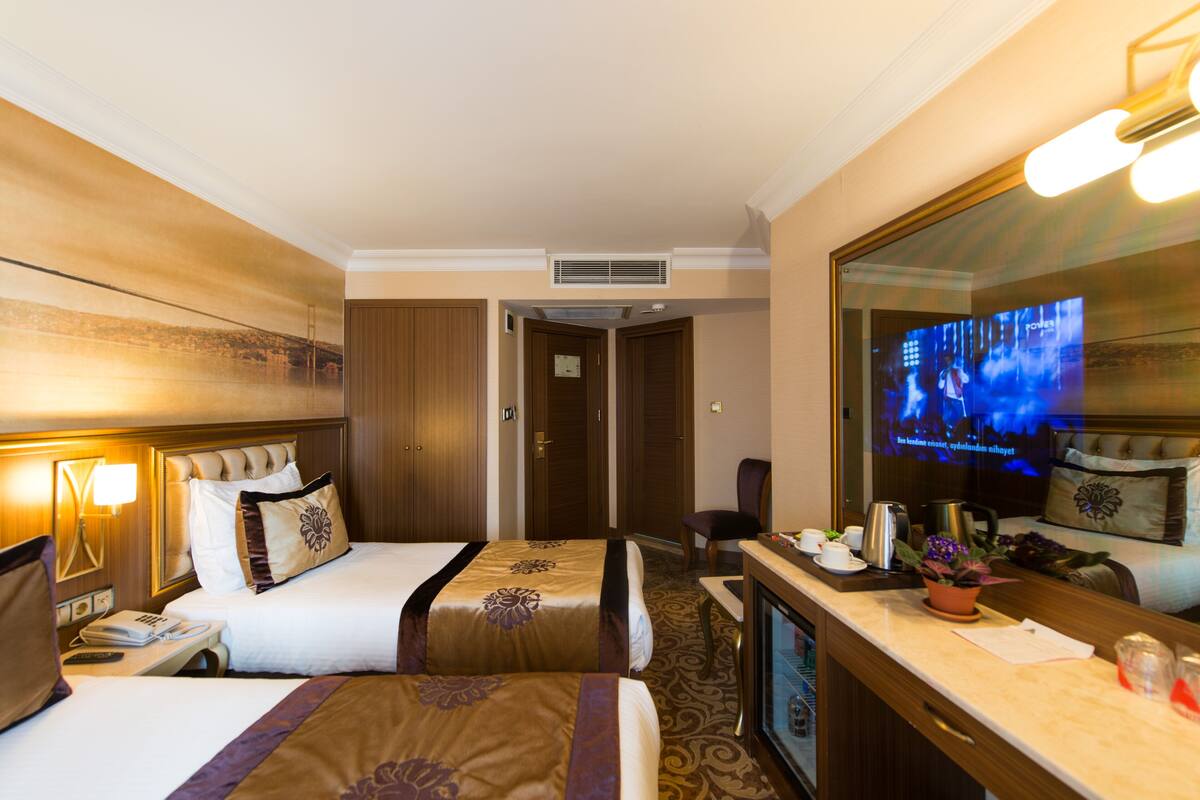 Ein Hotelzimmer mit zwei Betten, einem Schreibtisch mit Kaffeemaschine, einem Fernseher und einem großen Spiegel.