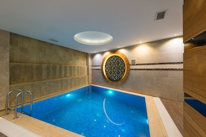 Uma piscina com piso em azulejo, um detalhe decorativo circular na parede e um aparelho de iluminação no teto.
