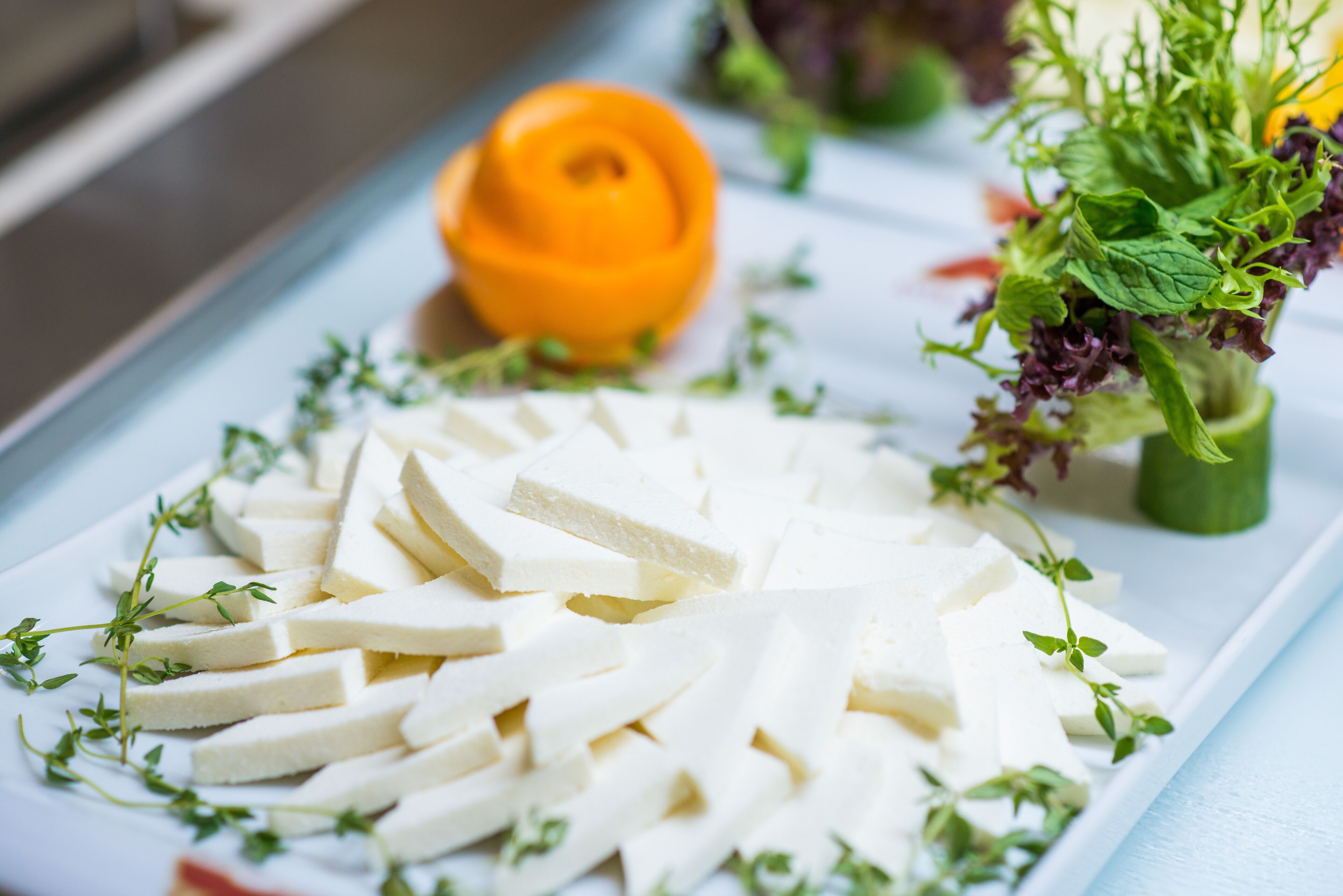 A white plate with sliced white cheese, garnished with green herbs, on a light blue tablecloth.