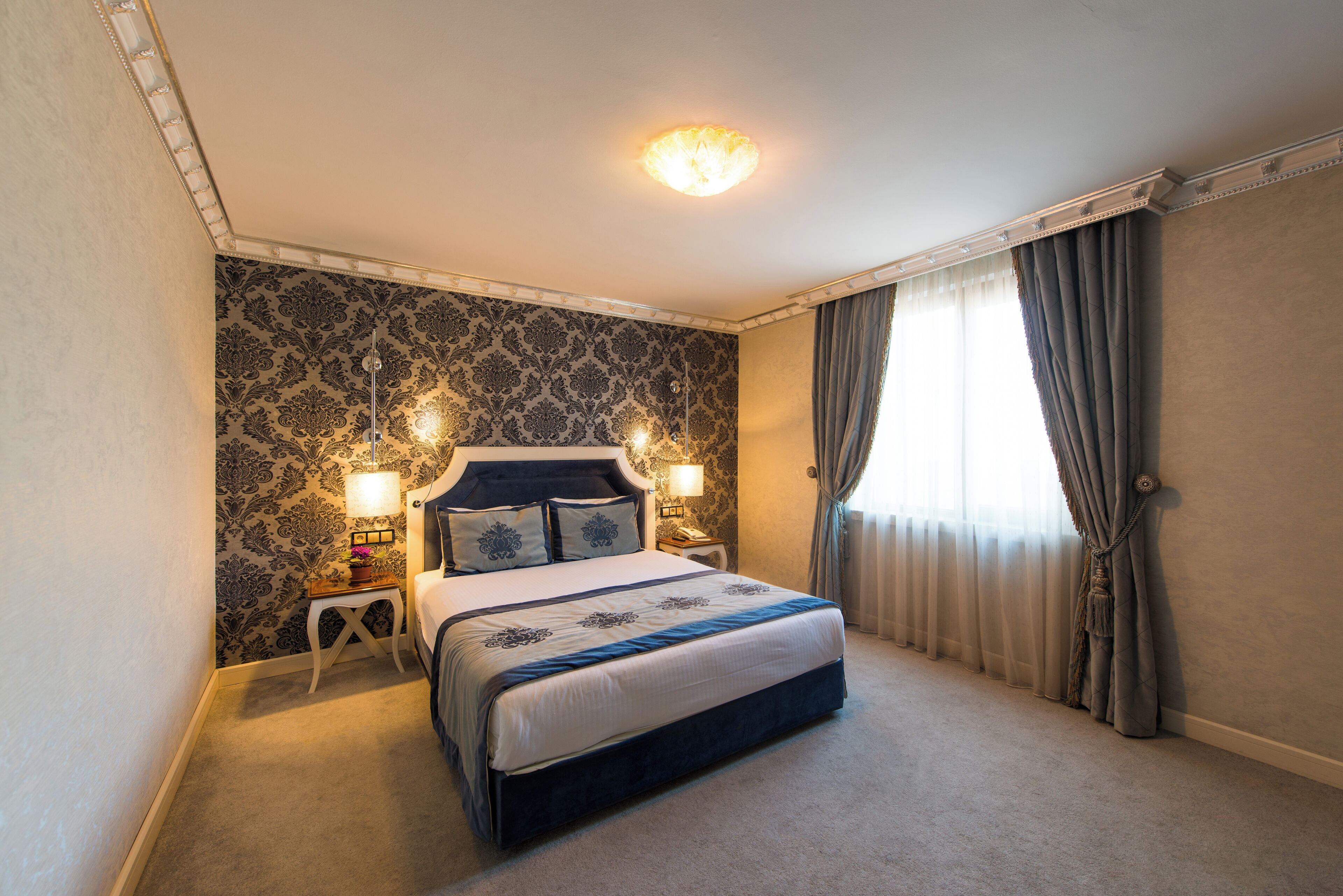 Une chambre à coucher bien aménagée, avec un grand lit, deux tables de chevet dotées de lampes et un papier peint à motifs.