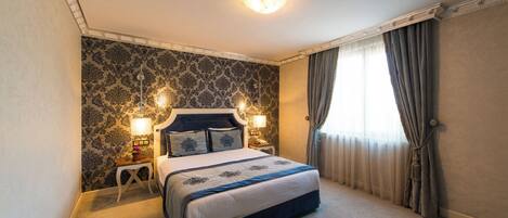 Une chambre à coucher bien aménagée, avec un grand lit, deux tables de chevet dotées de lampes et un papier peint à motifs.