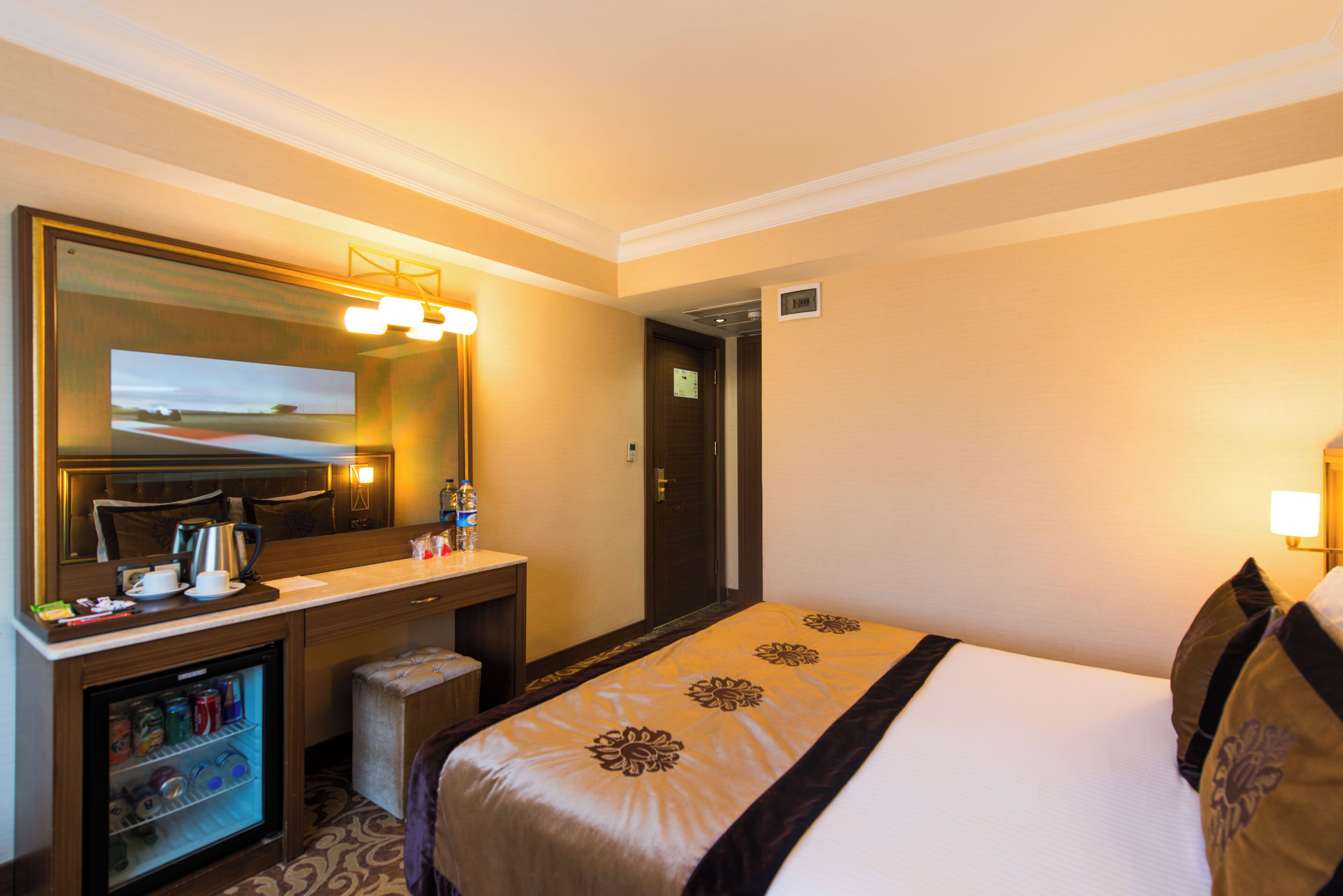 Habitación de hotel con cama, escritorio con espejo, minibar y puerta que da a otra habitación.