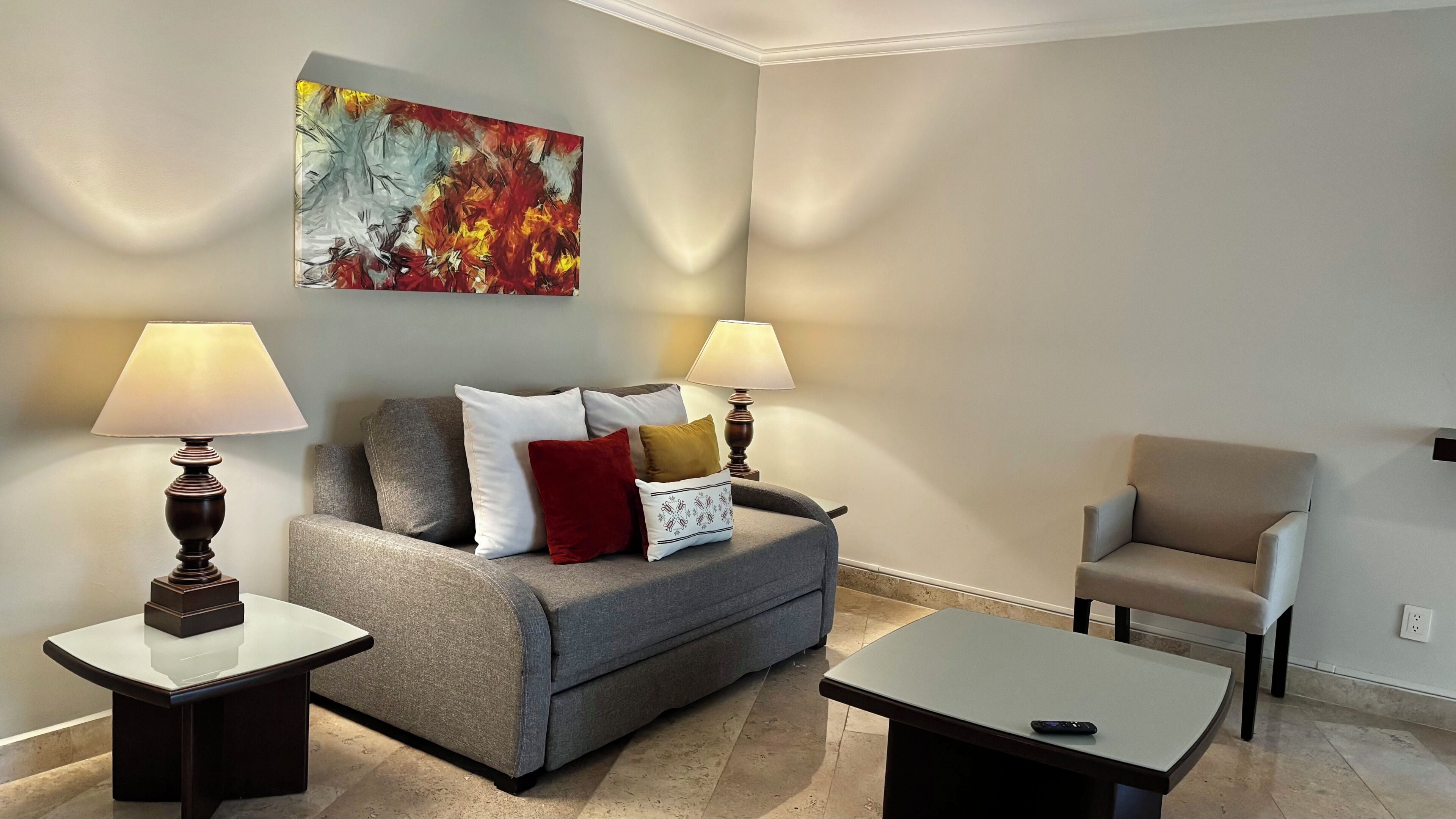 Un salon moderne avec un canapé gris, deux fauteuils, une table basse et deux lampes.