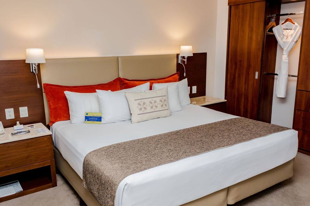 Une chambre d’hôtel comprenant un lit, des tables de chevet, une armoire en bois et un peignoir suspendu.