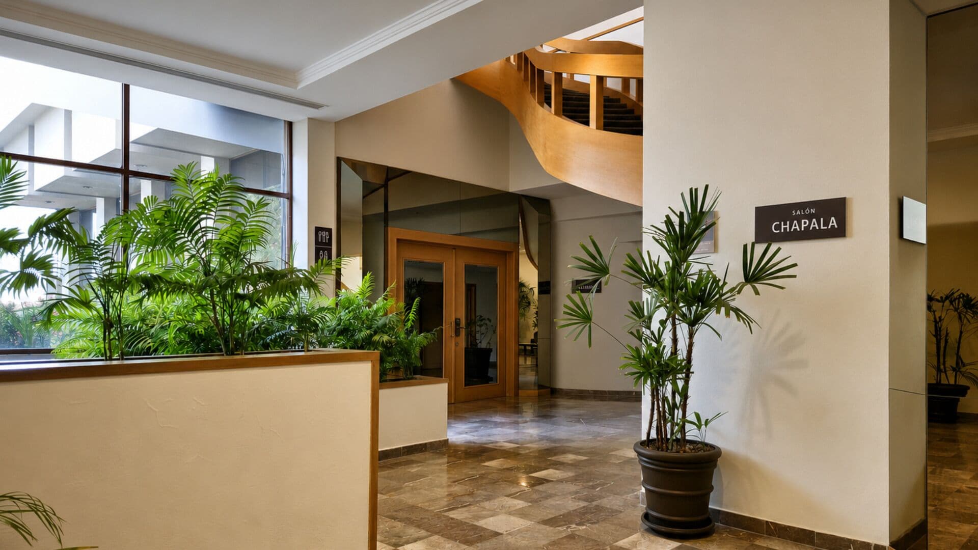 A hotel lobby with a checkered floor, a staircase, and potted plants.