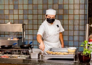 Un chef, vêtu d'un uniforme blanc, prépare des plats à un buffet, en utilisant divers ingrédients et ustensiles de cuisine.