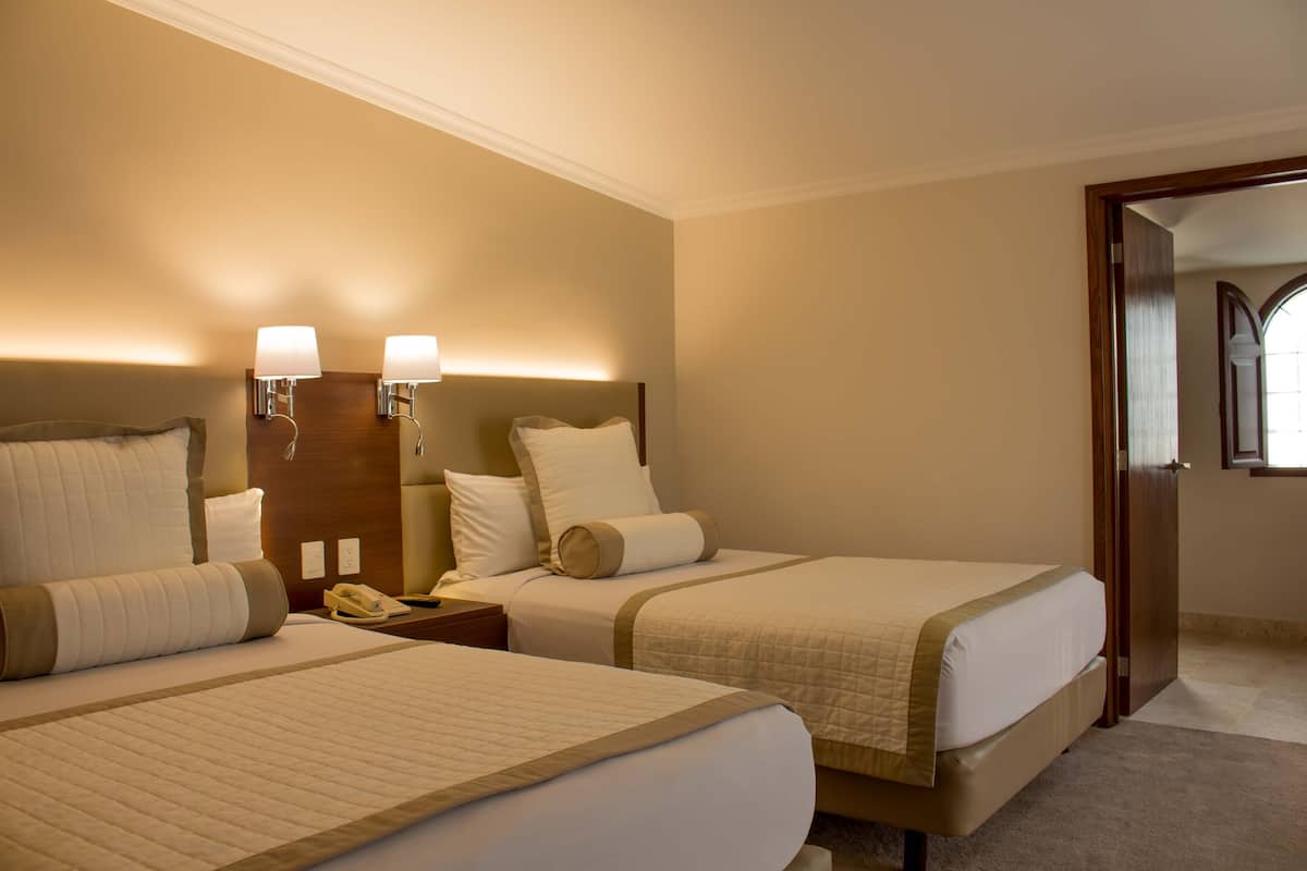 Une chambre d’hôtel avec deux lits, une table de chevet avec un téléphone et une tête de lit en bois.